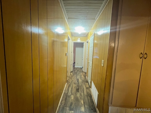 corridor with a textured ceiling, dark hardwood / wood-style floors, and wood walls