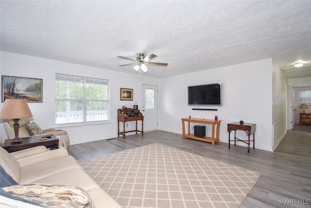 living room with a textured ceiling, dark wood-type flooring, and ceiling fan