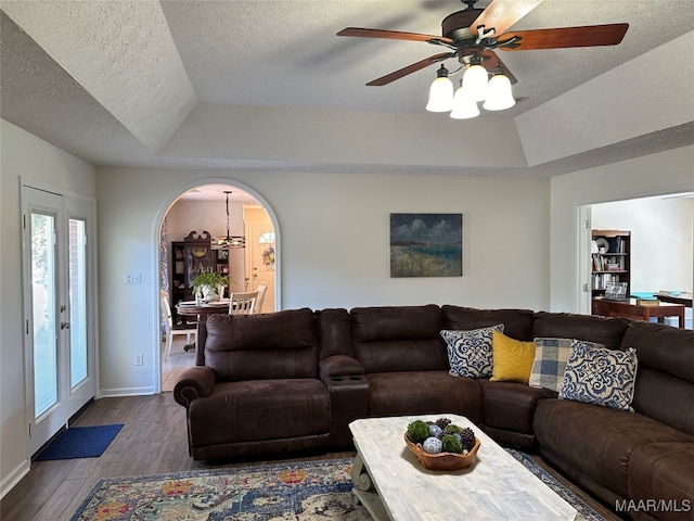 living room with ceiling fan with notable chandelier, hardwood / wood-style flooring, a raised ceiling, and a textured ceiling