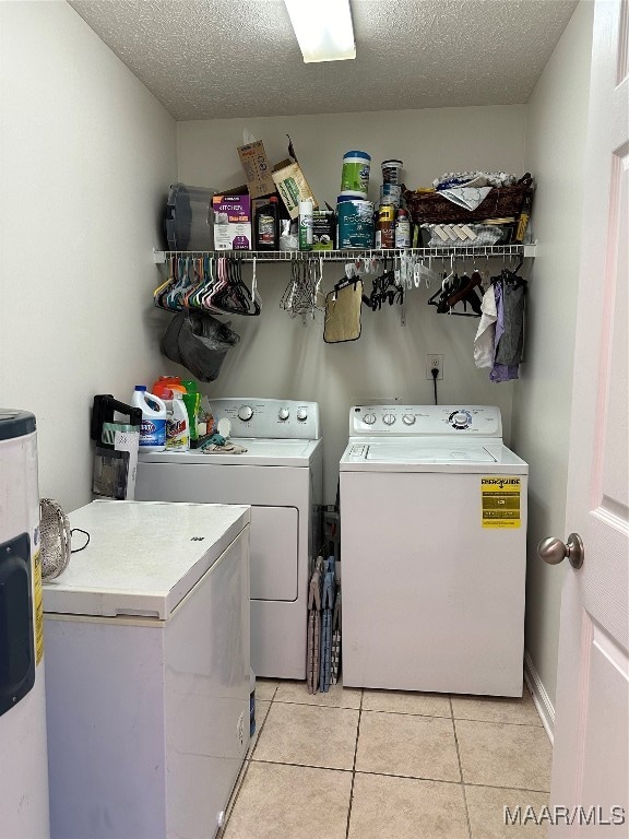 washroom with a textured ceiling, light tile patterned floors, washing machine and clothes dryer, and electric water heater