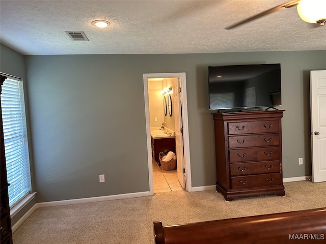 bedroom featuring ceiling fan, a textured ceiling, ensuite bath, and light carpet