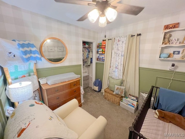 bedroom with a wainscoted wall, light carpet, ceiling fan, and wallpapered walls