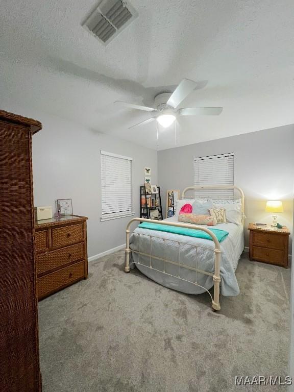 bedroom featuring visible vents, a ceiling fan, light carpet, a textured ceiling, and baseboards