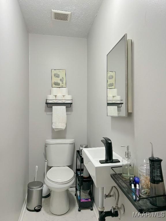 half bathroom with a textured ceiling, toilet, visible vents, baseboards, and marble finish floor