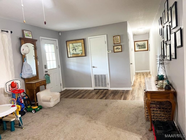 carpeted entryway with baseboards, visible vents, and wood finished floors