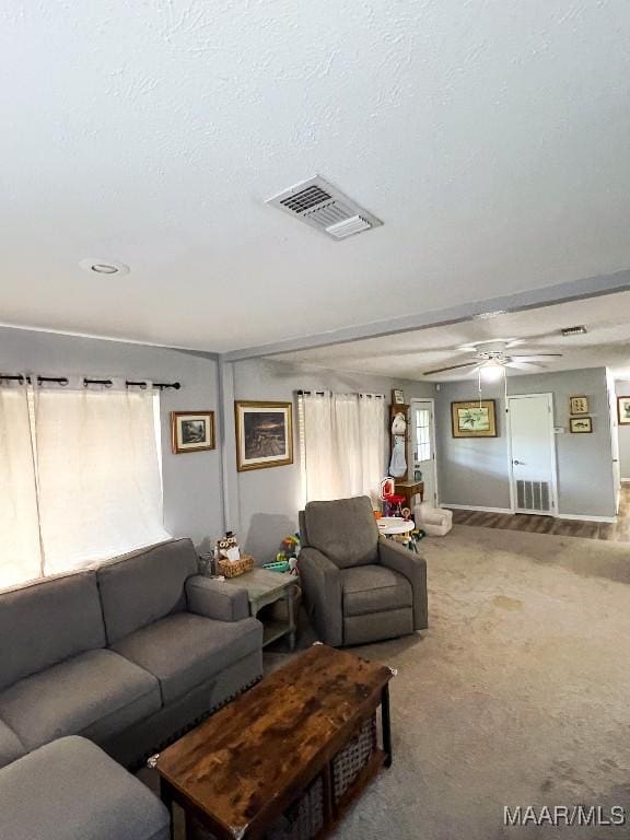 carpeted living room featuring a textured ceiling, visible vents, and a ceiling fan