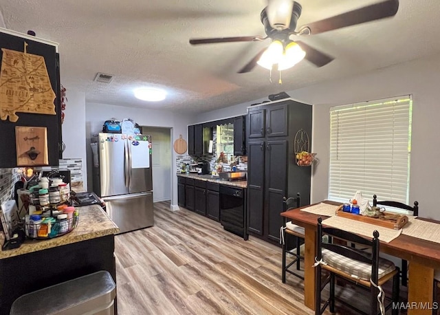 kitchen featuring visible vents, dark cabinets, freestanding refrigerator, a textured ceiling, and light wood-style floors