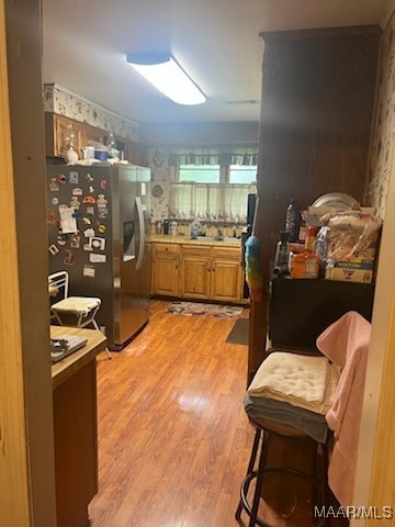 kitchen with stainless steel fridge, light hardwood / wood-style floors, and a kitchen bar