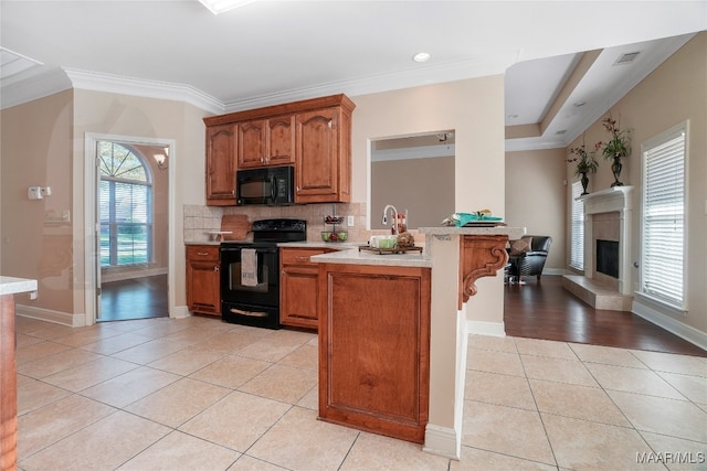 kitchen featuring tasteful backsplash, kitchen peninsula, black appliances, light hardwood / wood-style flooring, and ornamental molding