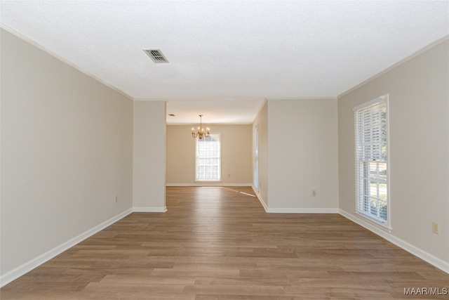 unfurnished room with a chandelier, light wood-type flooring, and ornamental molding