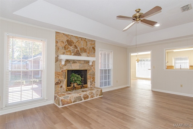 unfurnished living room with a raised ceiling, light hardwood / wood-style flooring, ceiling fan, and a stone fireplace