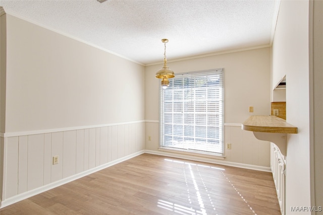 unfurnished dining area featuring a textured ceiling, light wood-type flooring, and ornamental molding