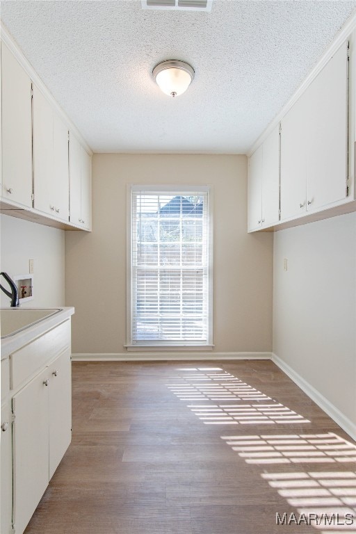 laundry room featuring cabinets, sink, hookup for a washing machine, light hardwood / wood-style flooring, and a textured ceiling