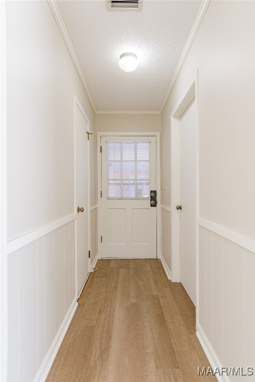 doorway with wooden walls, ornamental molding, a textured ceiling, and light wood-type flooring