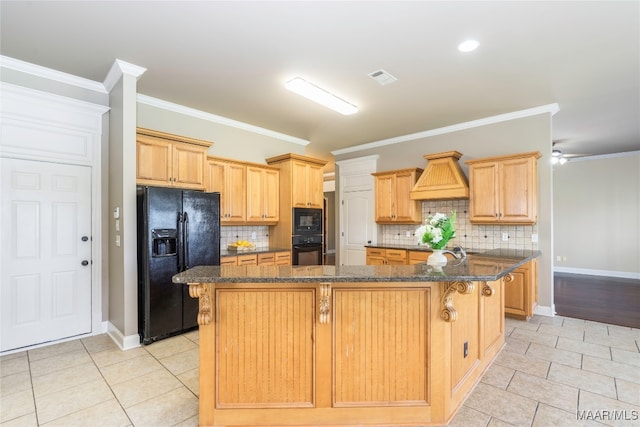 kitchen with a center island with sink, black appliances, dark stone countertops, crown molding, and decorative backsplash