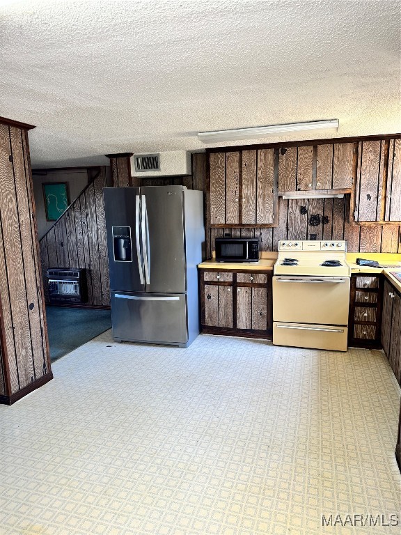 kitchen with a textured ceiling, wooden walls, white electric range, and stainless steel fridge with ice dispenser