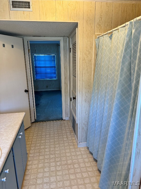 bathroom with walk in shower, vanity, wood walls, and a textured ceiling