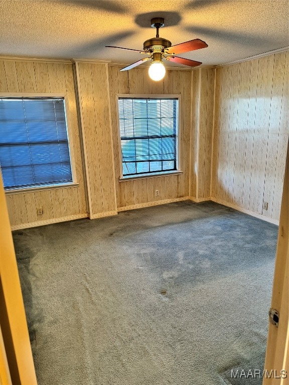 carpeted spare room featuring wood walls, ceiling fan, and a textured ceiling