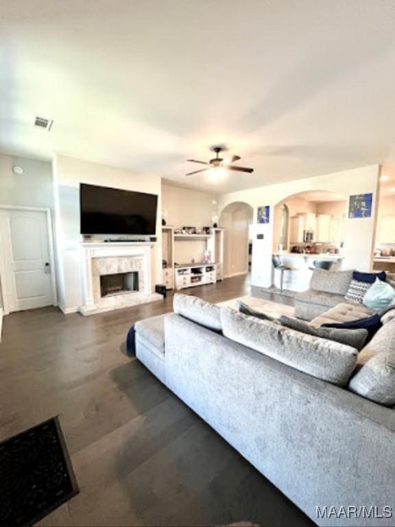 living room with arched walkways, a ceiling fan, and a high end fireplace