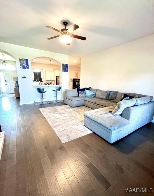 living area with arched walkways, a ceiling fan, and dark wood-type flooring