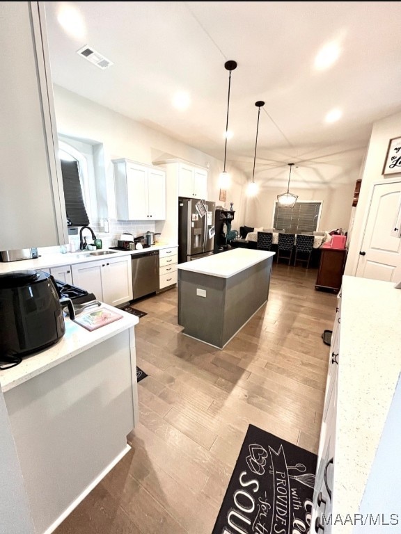 kitchen with pendant lighting, a kitchen island, white cabinetry, stainless steel appliances, and light hardwood / wood-style floors