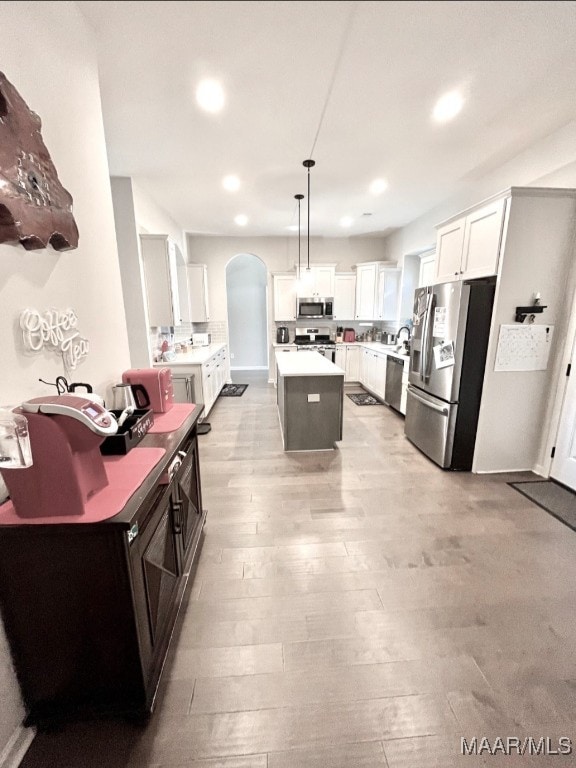 kitchen with white cabinets, decorative light fixtures, light hardwood / wood-style flooring, appliances with stainless steel finishes, and a center island