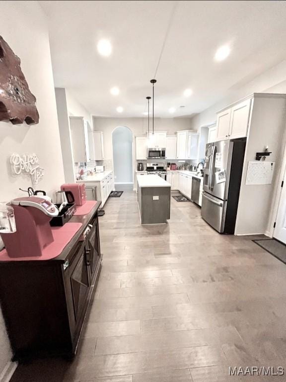 kitchen featuring appliances with stainless steel finishes, arched walkways, a kitchen island, light wood-style floors, and white cabinets