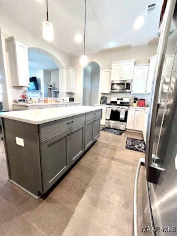 kitchen with appliances with stainless steel finishes, gray cabinetry, arched walkways, light countertops, and white cabinetry