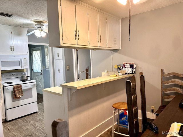 kitchen with white cabinetry, white appliances, kitchen peninsula, a breakfast bar area, and ceiling fan