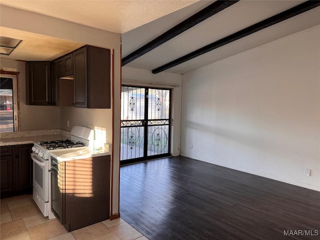 kitchen with dark brown cabinetry, beam ceiling, white gas stove, and light tile patterned floors