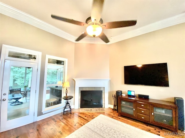 living room with crown molding, a tile fireplace, light wood-type flooring, and ceiling fan