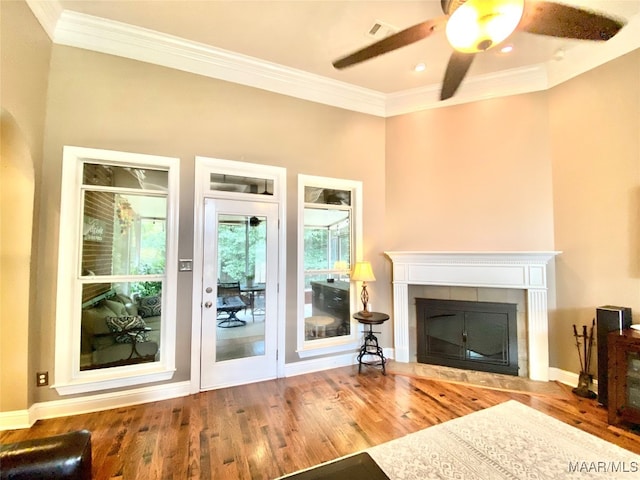 unfurnished living room featuring ceiling fan, wood-type flooring, ornamental molding, and a tile fireplace