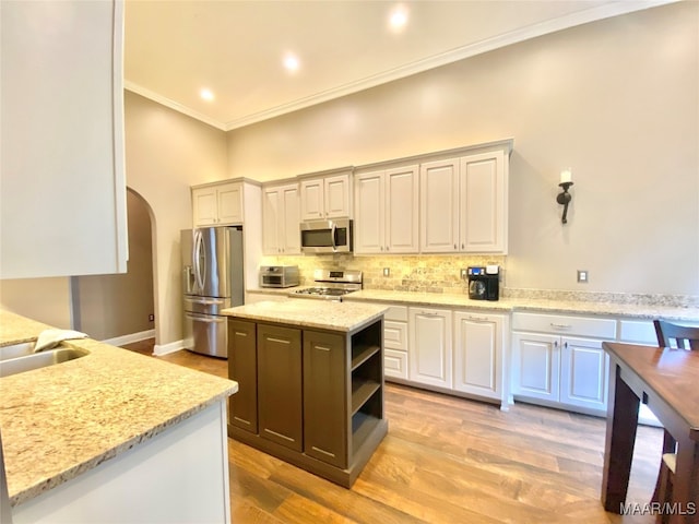 kitchen featuring a kitchen island, appliances with stainless steel finishes, light stone countertops, light hardwood / wood-style flooring, and ornamental molding