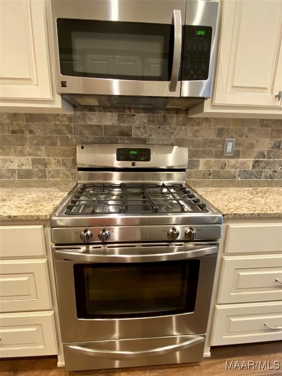 kitchen featuring appliances with stainless steel finishes, decorative backsplash, light stone countertops, and white cabinetry