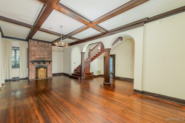 unfurnished living room featuring a brick fireplace, beamed ceiling, wood-type flooring, coffered ceiling, and a notable chandelier