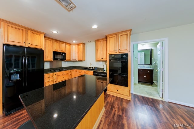 kitchen with dark stone counters, black appliances, dark wood-type flooring, and sink