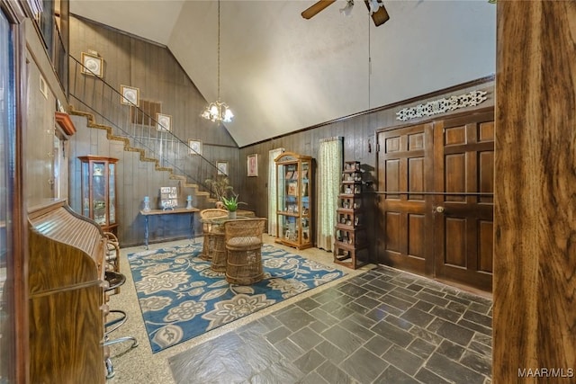 entrance foyer with high vaulted ceiling, ceiling fan with notable chandelier, and wooden walls