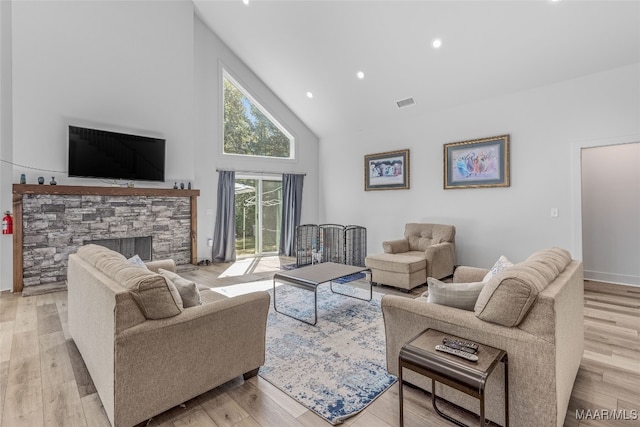 living room featuring high vaulted ceiling, light hardwood / wood-style floors, and a stone fireplace