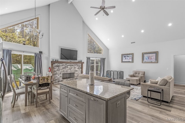 kitchen featuring high vaulted ceiling, light wood-type flooring, light stone counters, and a stone fireplace