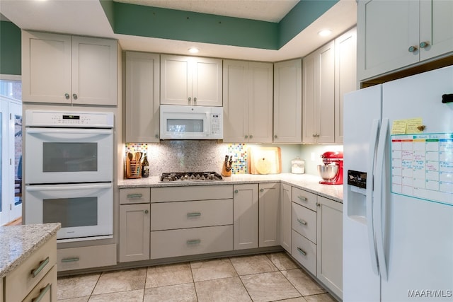 kitchen featuring decorative backsplash, white appliances, light stone counters, and light tile patterned floors