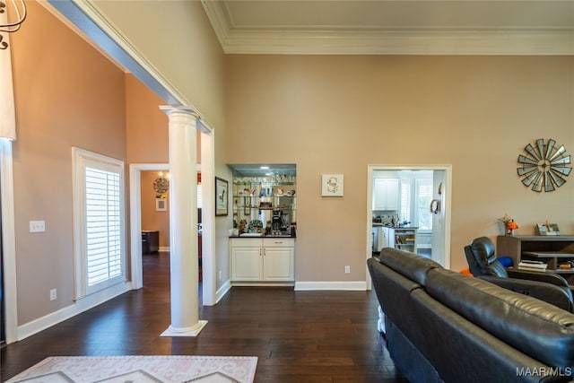 living room featuring a towering ceiling, dark hardwood / wood-style floors, ornate columns, and a wealth of natural light