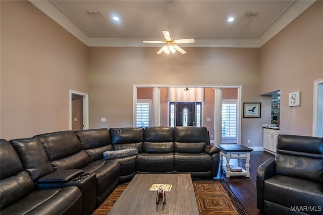 living room with a high ceiling, ceiling fan, ornamental molding, ornate columns, and dark hardwood / wood-style flooring