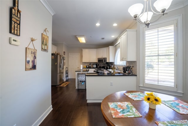 kitchen with appliances with stainless steel finishes, crown molding, pendant lighting, an inviting chandelier, and white cabinetry