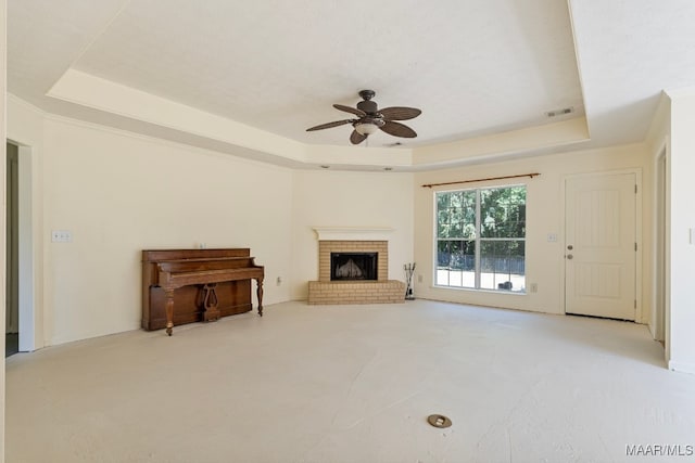 unfurnished living room featuring a brick fireplace, ceiling fan, and a raised ceiling