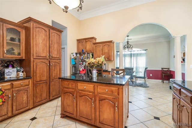 kitchen with light tile patterned flooring, a kitchen island, crown molding, and dark stone counters