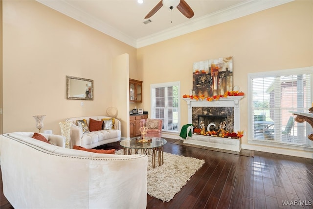 living room featuring a high ceiling, ceiling fan, crown molding, dark wood-type flooring, and a fireplace