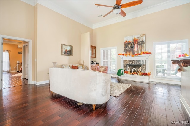 living room featuring ceiling fan, a high end fireplace, crown molding, dark hardwood / wood-style floors, and a towering ceiling