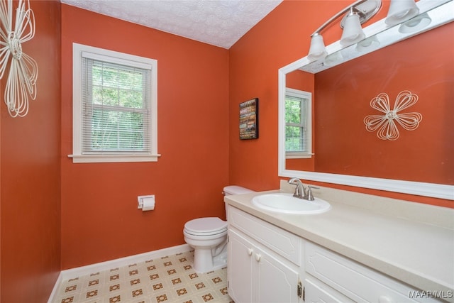 bathroom with a textured ceiling, plenty of natural light, vanity, and toilet