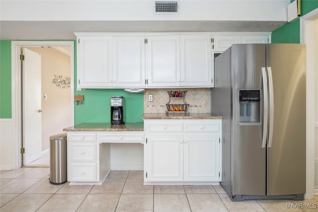 kitchen featuring light stone counters, tasteful backsplash, stainless steel fridge, light tile patterned flooring, and white cabinetry