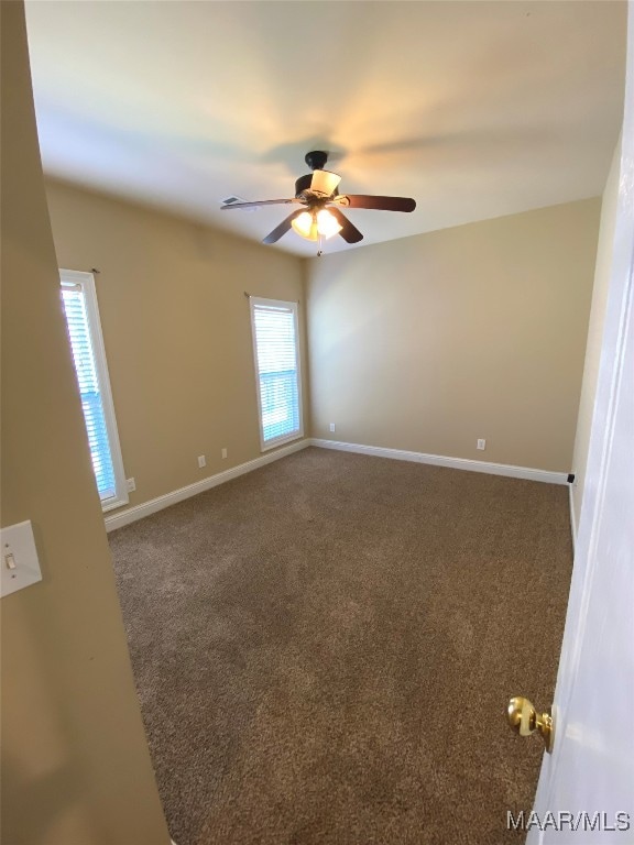 empty room featuring ceiling fan and dark carpet